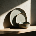 A large ribbed-rim plate propped upright on an oak shelf with a bowl and small plate stacked in front.