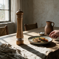 Tall oak grinder standing on a laid dining table beside a stoneware plate and linen napkin.