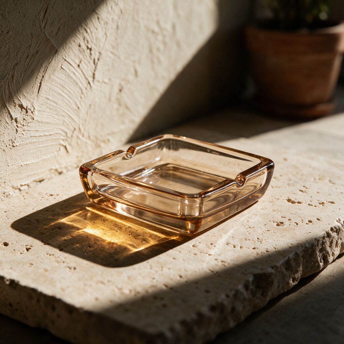 Empty amber glass tray on a travertine slab casting a warm caustic patch of light.