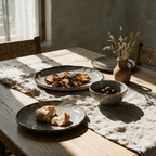 Speckled stoneware platter, plates and bowl laid for a meal on an oak dining table.