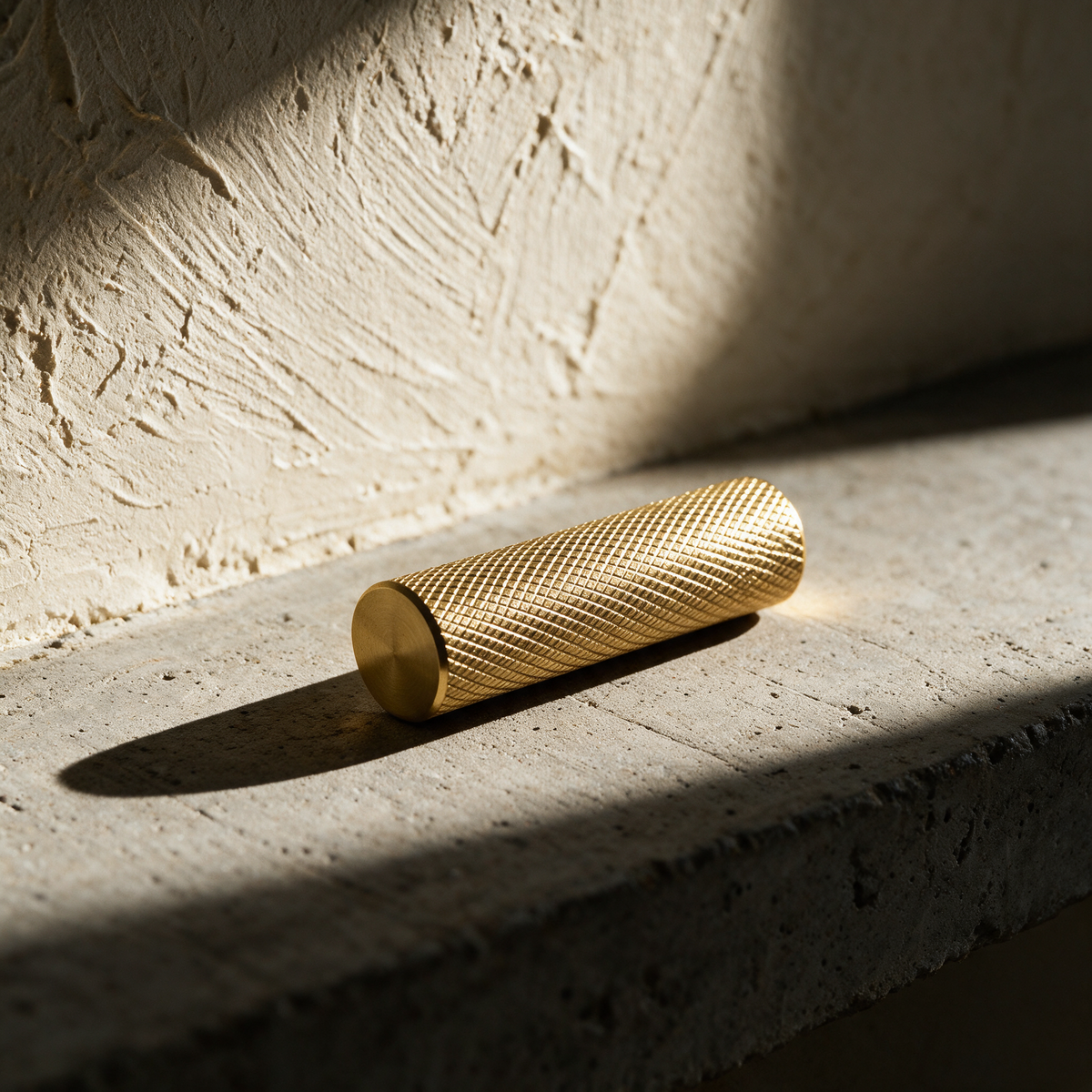 A single knurled brass handle lying on a concrete slab in hard raking light.
