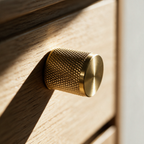 Macro view of a small knurled solid brass cabinet knob on an oak drawer front.