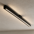 Close view of a slim matte black linear ceiling light glowing against a plaster ceiling