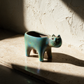 The empty cat planter alone on a travertine slab against a textured plaster wall.
