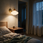 Brass gooseneck wall light glowing above a walnut bedside table in a dusk-lit bedroom.