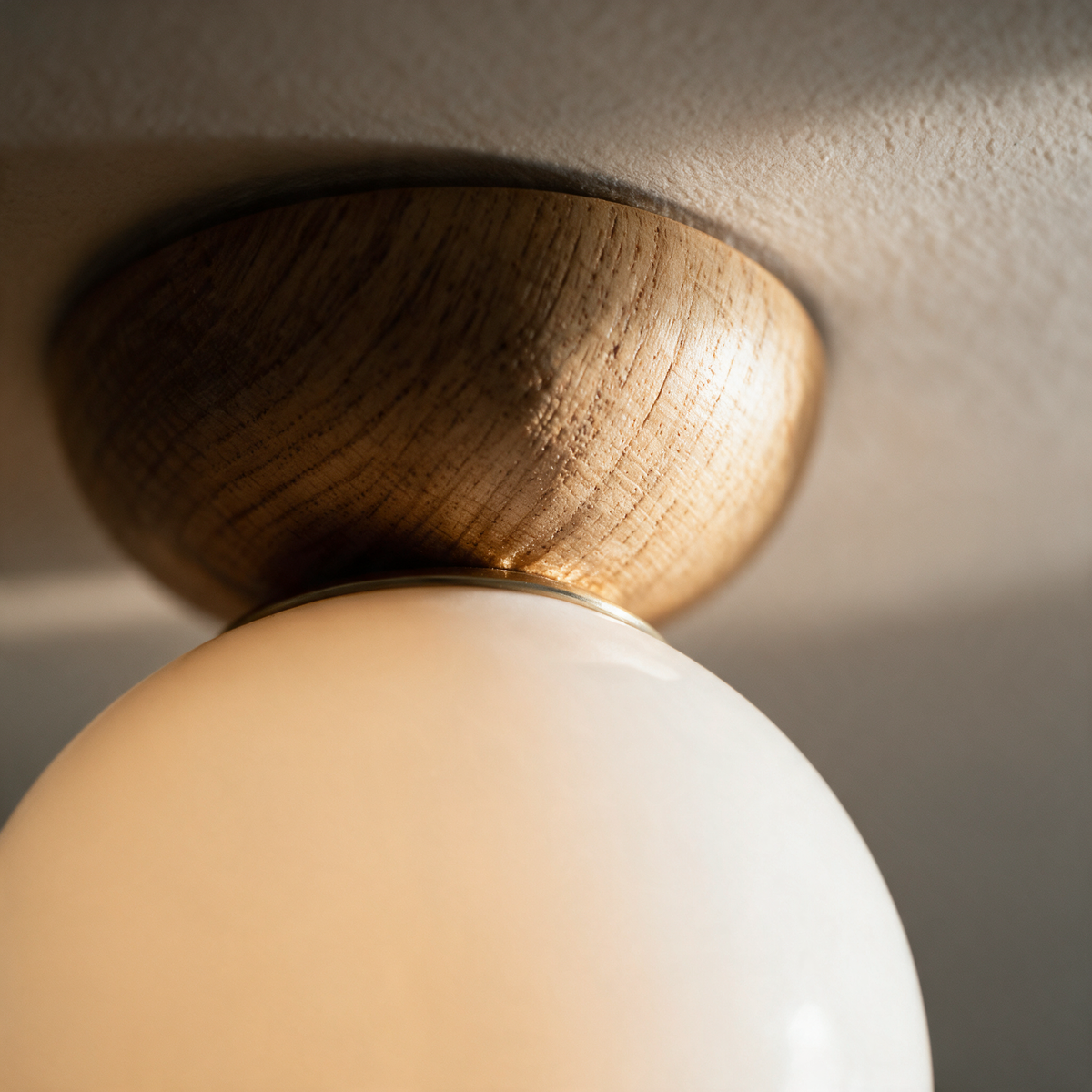Macro close-up of the seam where the opal glass globe meets the turned timber canopy.