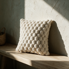 The bobble cushion standing alone on an oak bench against a plaster wall in raking sunlight.