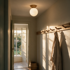 Side profile of the lit globe ceiling light in a hallway with coat pegs and an open door at golden hour.