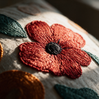 Macro detail of the dense stitching at the centre of an embroidered red poppy with a teal leaf.