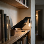 Side profile of the lit crow lamp on a pale oak bookshelf beside a row of books.