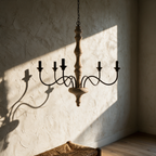 Unlit chandelier casting long spoked shadows of its iron arms across a textured plaster wall.