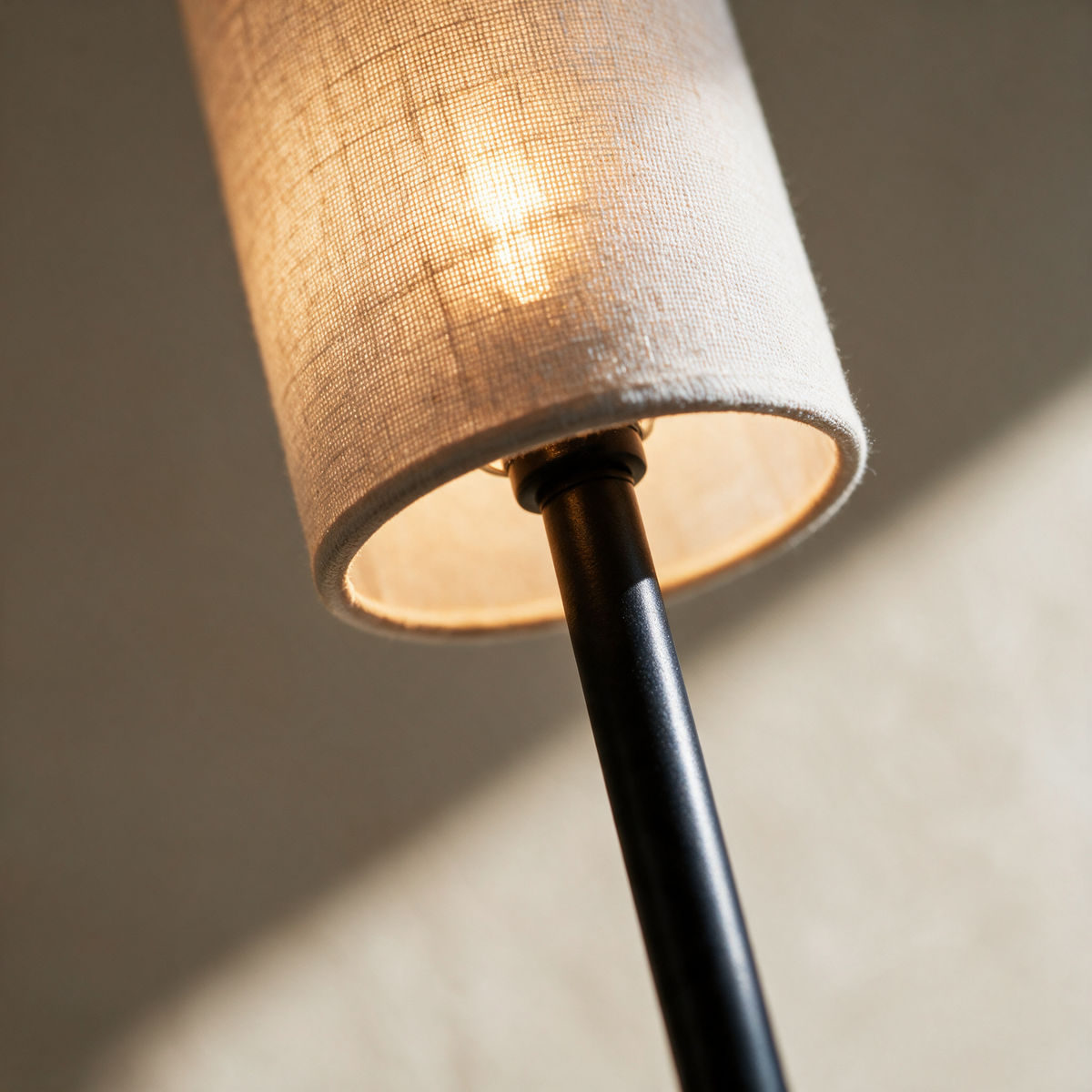 Close-up of the cream cylinder shade rim where the slim black stem enters it.