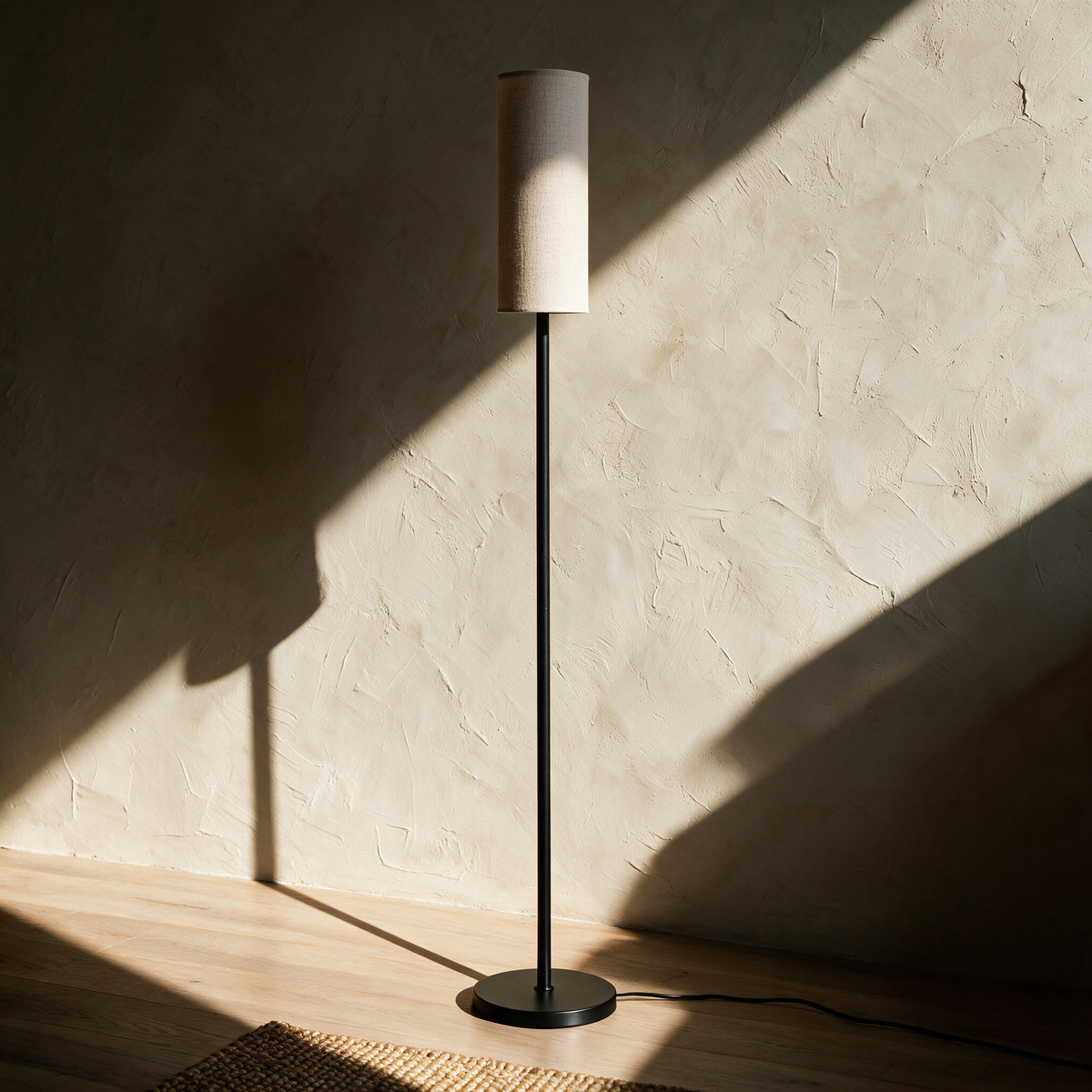 Unlit slim floor lamp on a pale oak floor casting a long line of shadow on plaster.