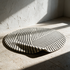 The round rug lying alone on a stone floor with one edge lifted to show the depth of the pile.