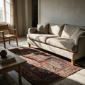 Large traditional patterned rug in red and blue under a linen sofa in a sunlit living room.