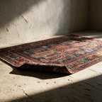 The patterned rug lying alone on a stone floor with one corner folded back in raking sunlight.