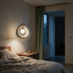 Textured resin pebble pendant lit beside a linen bed in a plaster-walled bedroom at dusk.