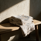 The mandala throw folded in a loose stack on an oak bench against a plaster wall.
