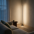 Slim glowing LED rod floor lamp lighting a living room corner at dusk.
