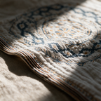 Macro detail of the blue mandala petals against the cream cotton weave near a hemmed edge.