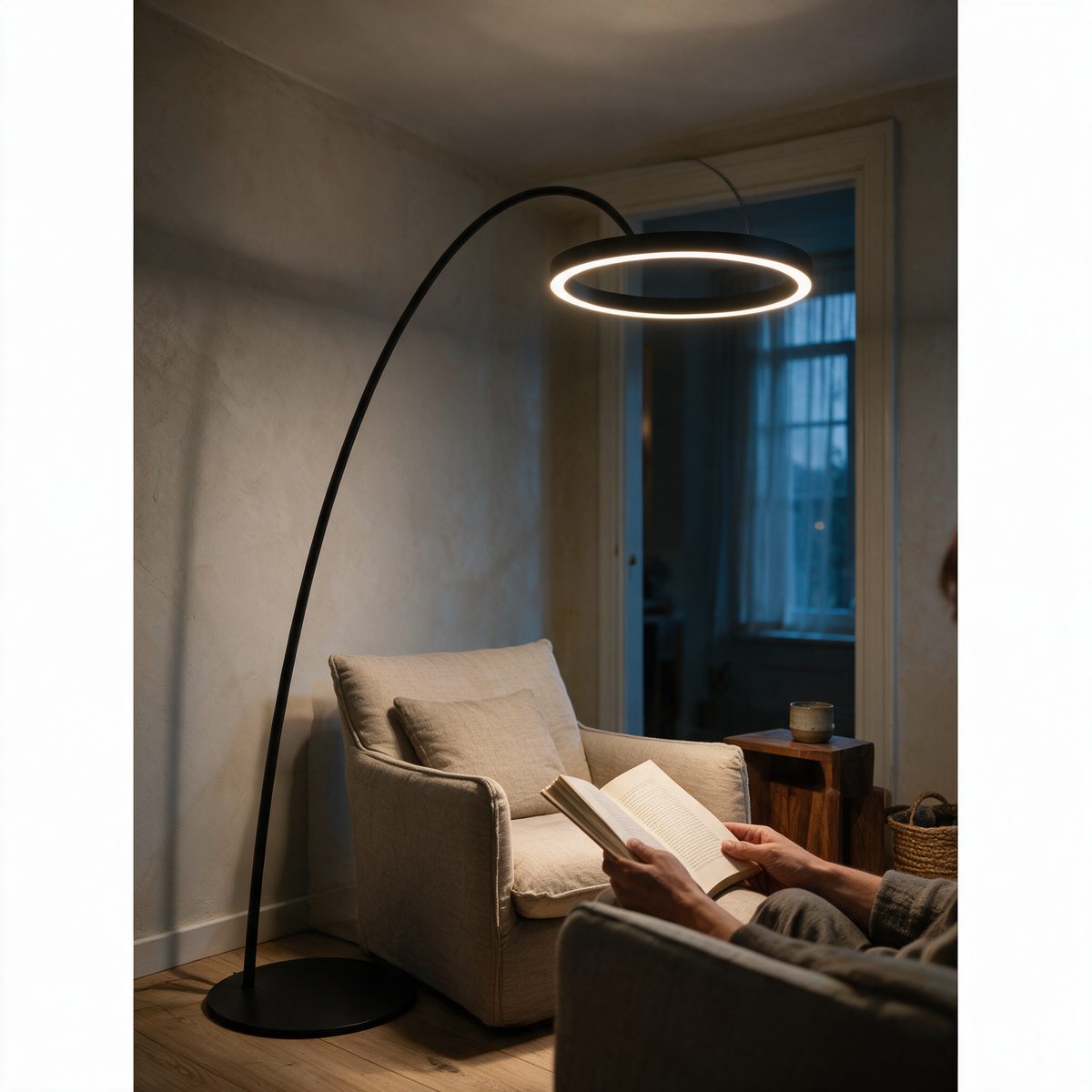 Arc floor lamp with a glowing ring lighting a reader in an armchair at dusk.