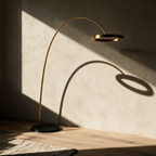 Unlit gold arc lamp casting a curved shadow with a circle on a plaster wall.