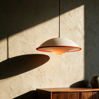 Unlit saucer pendant casting a long elliptical shadow across a textured plaster wall.
