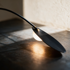 Macro close-up of a glowing leaf blade meeting the slim black arm with a gold accent at the joint.