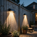 Two black wedge solar downlights on a timber garden fence washing warm triangles of light at dusk.