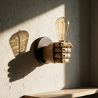 Unlit fist sconce casting a sharp shadow of its fingers and bulb across a textured plaster wall.
