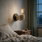 Side profile of the lit fist sconce projecting from a bedroom wall above a bedside table.