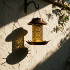Unlit hanging lantern on an iron hook casting a long shadow on a plaster wall.