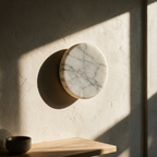Unlit veined stone disc flush to a plaster wall with raking afternoon sun showing its grey veining.