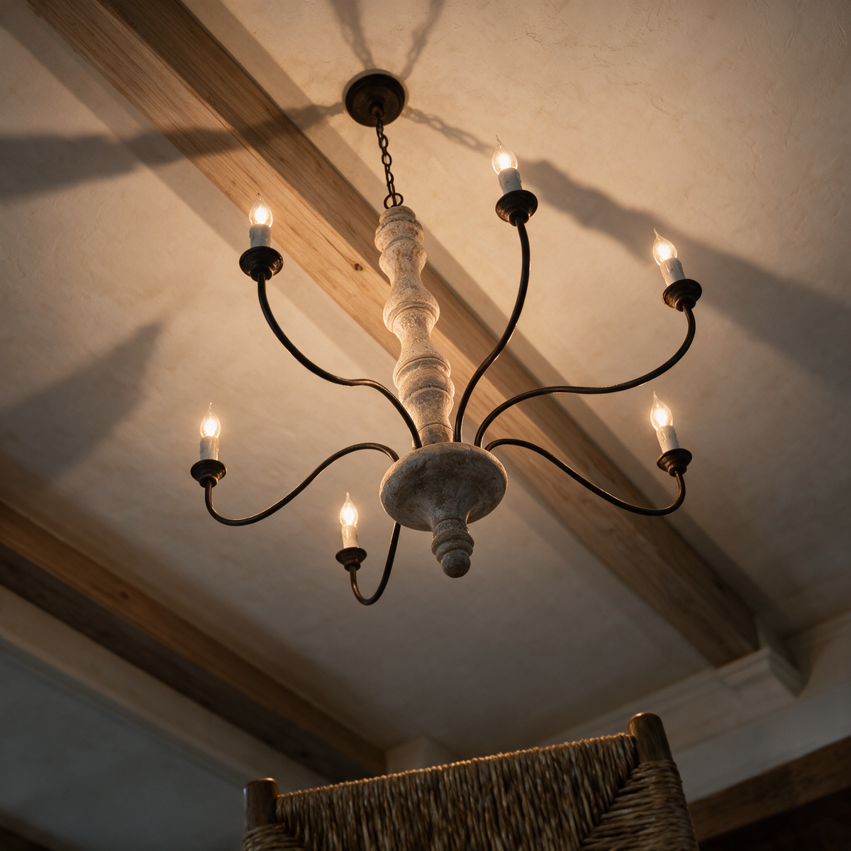 A wood and iron candle chandelier seen from below against a plaster ceiling and timber beam.