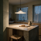 A single clear glass disc pendant light lit above a stone kitchen island at dusk.