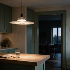 A clear glass disc pendant light seen in profile above a timber kitchen bar.