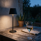 A cordless table lamp lit on a weathered timber terrace table at blue hour.