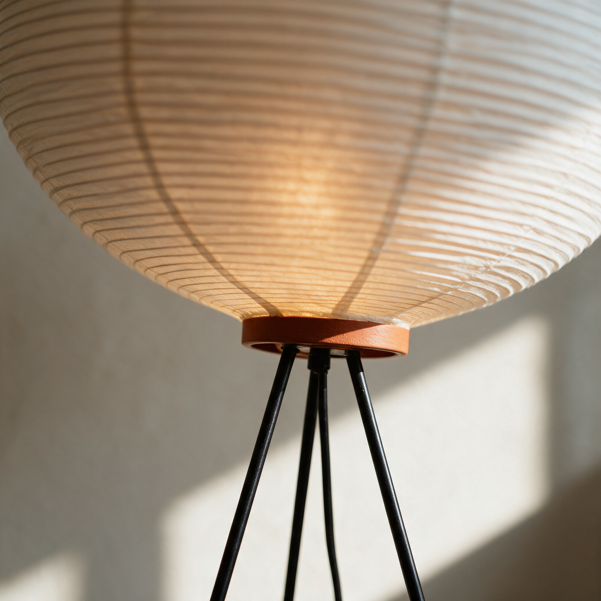 Close view of a rice paper globe floor lamp where the terracotta collar meets the three black tripod legs.