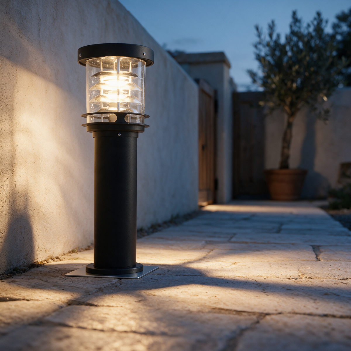 A single tiered louvred bollard light lit beside a stone garden path at dusk.