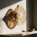 Unlit amber art glass wall light with a smooth round centre puck on a sunlit plaster wall