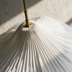 Close up of a pleated fabric pendant gathered under a thin brass band on a slim brass tube