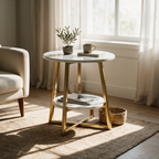 Round marble top side table with brass legs and a lower shelf beside an armchair in a sunlit living room
