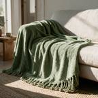 Pistachio green chenille throw with a tassel fringe draped over a cream sofa onto a jute rug