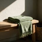 Folded green chenille throw with knotted tassels resting on a timber bench in sunlight